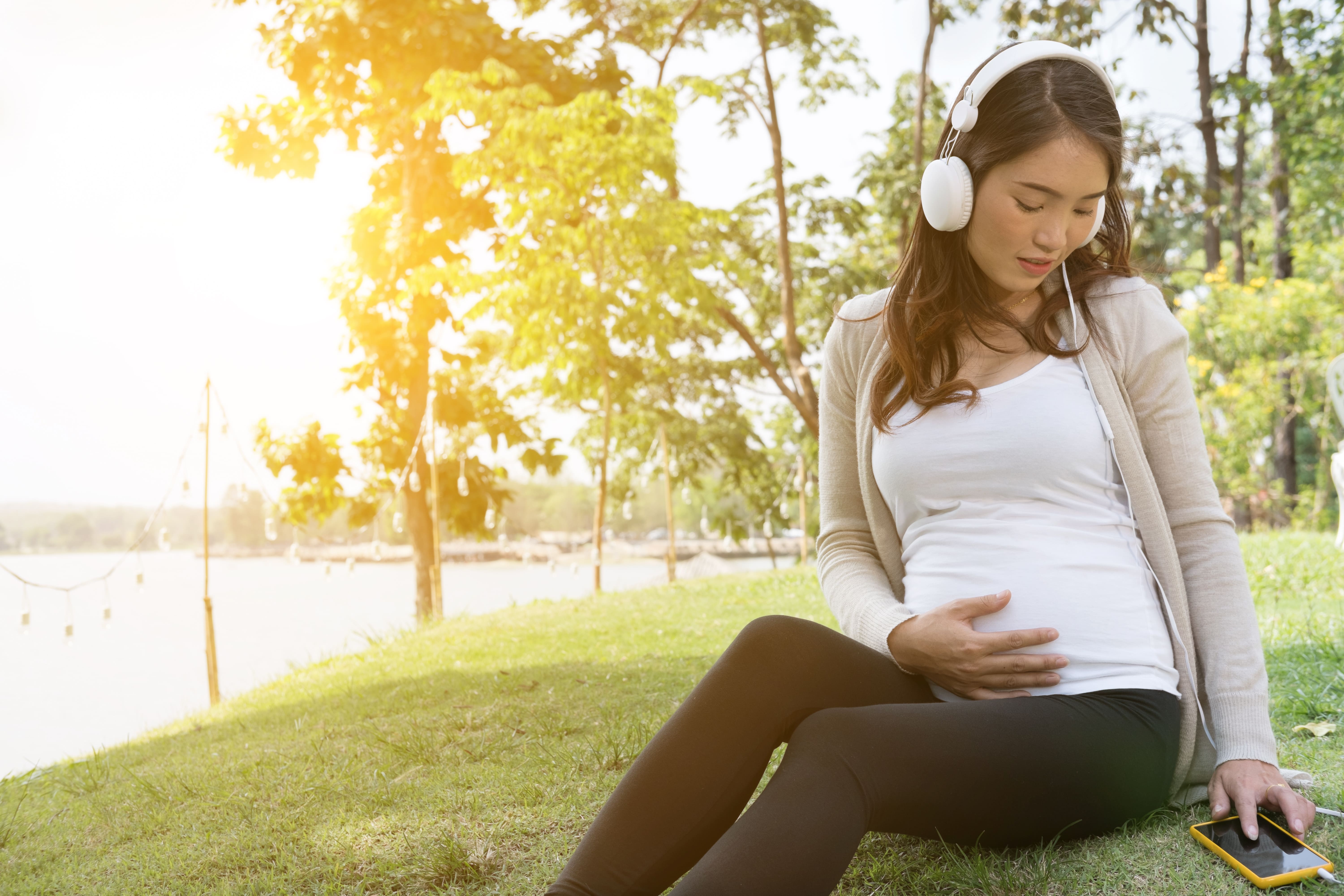pregnant-woman-listening-music-mobile-phone-while-sitting-grass.jpg