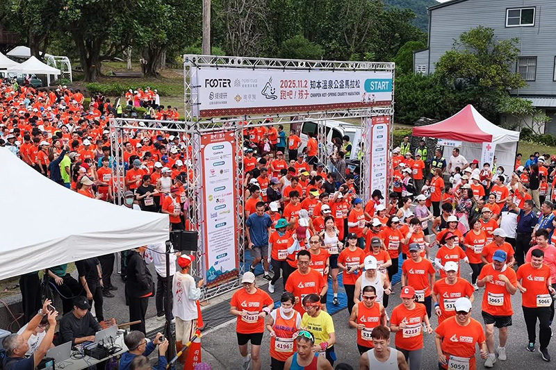 2025 知本溫泉公益馬拉松起跑盛況,眾多身穿橘色紀念衫的跑者熱情通過起跑拱門,現場氣氛熱鬧非凡,展現台東知本的運動活力。