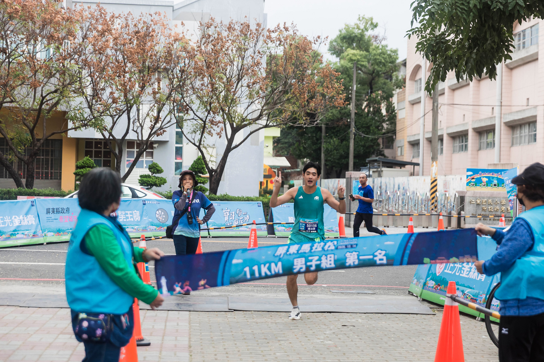 屏東馬拉松終點畫面，11 公里組跑者衝線完成比賽，工作人員於終點拉起完賽布條，賽道周邊設有補給與動線引導，現場氣氛緊張又熱烈。