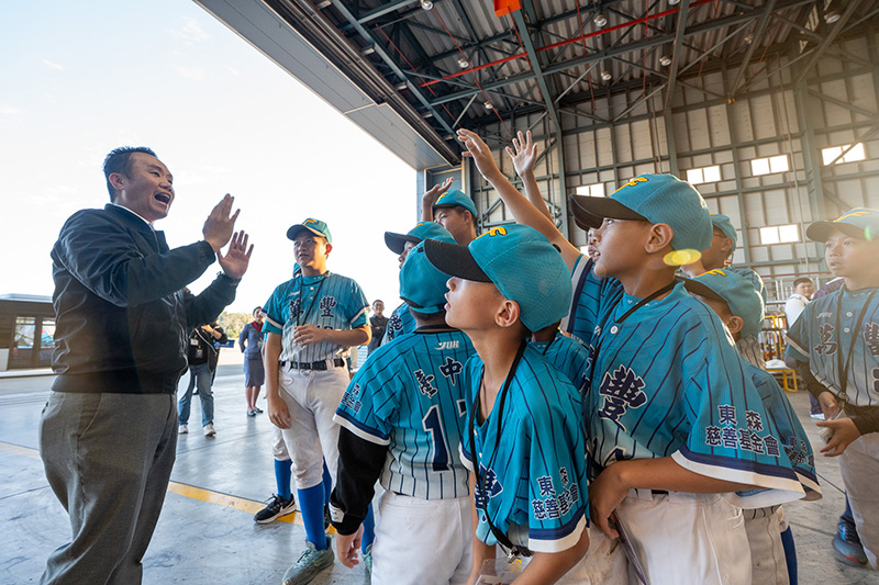 穿著棒球服的小球芽們在飛機棚廠內，抬頭專注聆聽航空職人解說工作內容，體驗航空產業職涯。象徵球芽基金會帶領孩子拓展視野，讓夢想一同起飛。