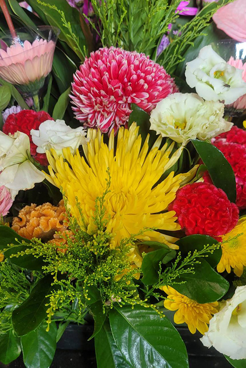 廟中祭祀插花作品,以鮮黃色、粉紅色與白色菊花為主角,搭配康乃馨、石竹花與綠葉植物點綴,色彩層次豐富,展現秋日花卉的溫暖與生命力。