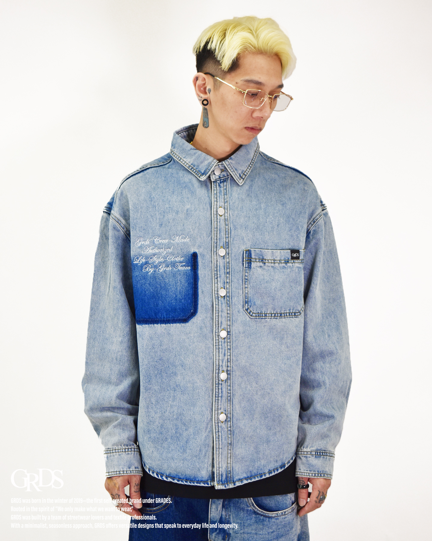 以「Cursive Embroidery」為設計核心，靈感源自自然波浪般草寫字跡，在牛仔布的穩重中注入動態筆觸。 襯衫沿用經典牛仔布料，以刺繡工藝在胸前勾勒流暢線條，展現書寫與材質之間的對話。 整體剪