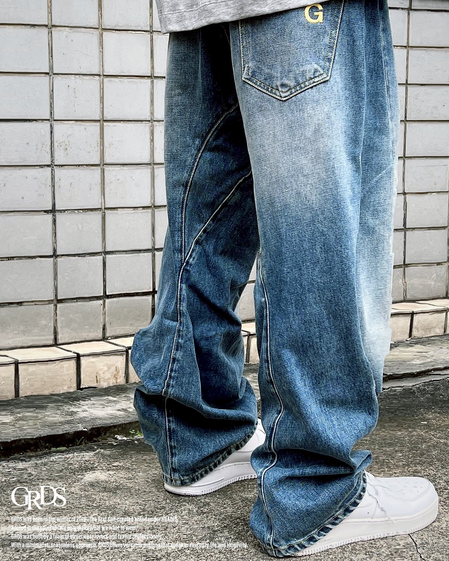 彎刀剪裁復古水洗牛仔褲  團隊以亞洲身型適配的錐形褲型為基礎開發， 透過前片斜向剪裁創造立體輪廓，帶出品牌標誌性的視覺語彙。 丹寧布料經中藍水洗工藝處理，展現自然褪色與柔和刷色， 輪廓寬鬆但不鬆垮，讓